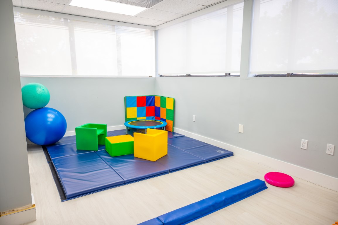 The pediatric therapy room at Peek A Boo PPEC with floor mats, a therapy ball, foam blocks and large windows
