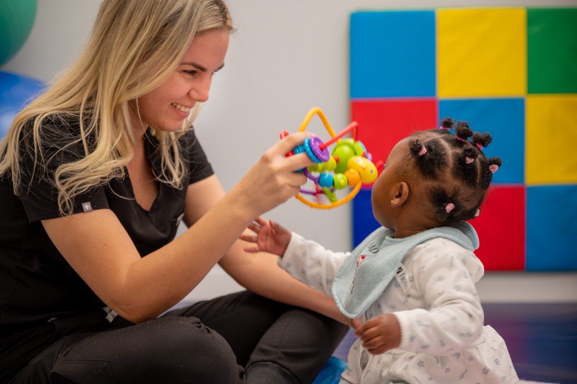 A nurse smiling and playing with a toddler using a colorful rattle at Peek A Boo PPEC